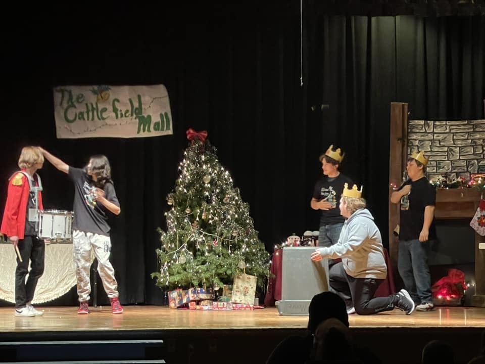 Students onstage with gold prop crowns and a Christmas Tree